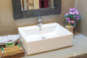 A bathroom with a white sink, a mirror, and a vase of purple flowers. - Moning Villa Ubud (Ubud)