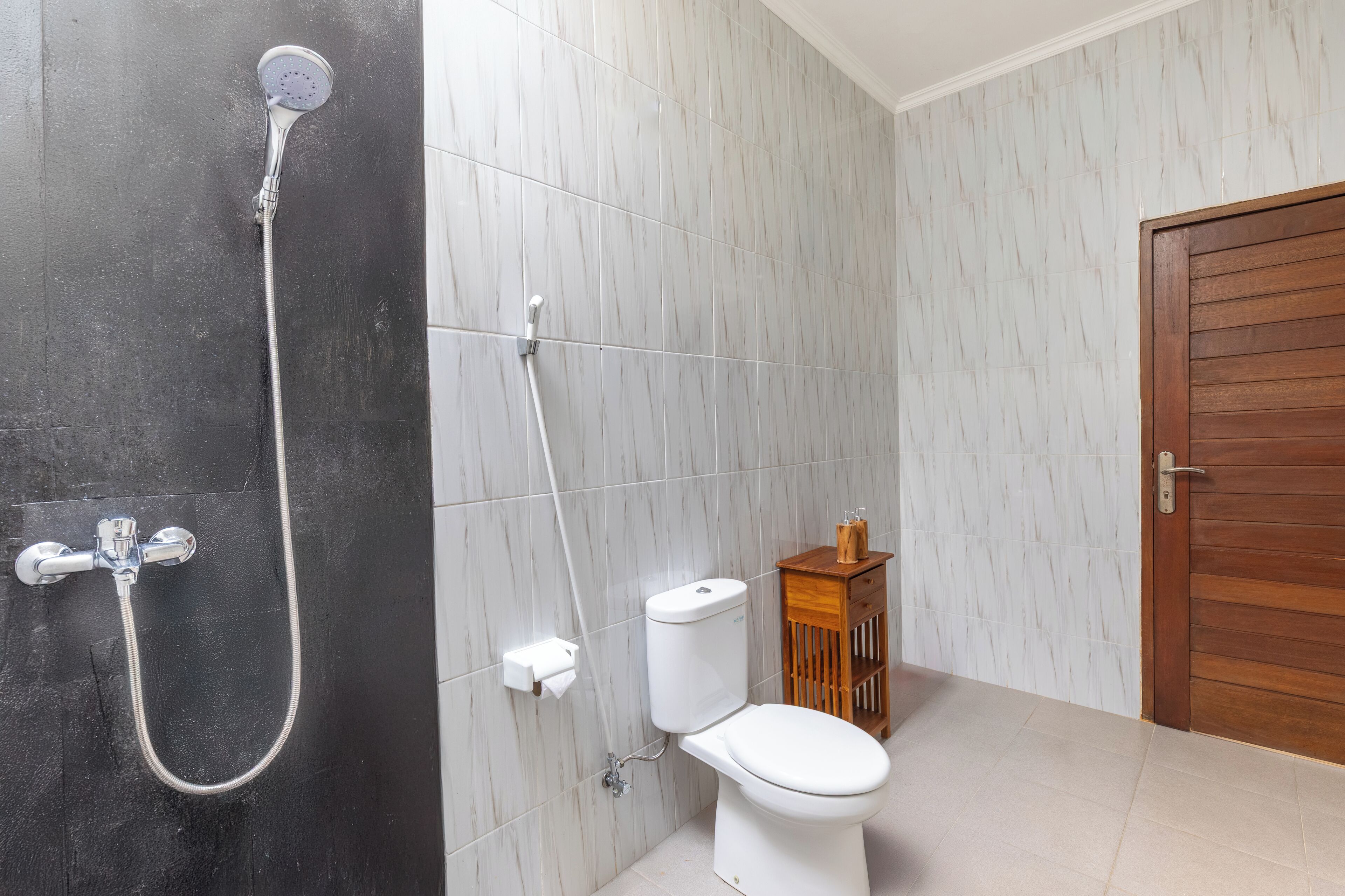 A bathroom with a shower, toilet, and a wooden cabinet.