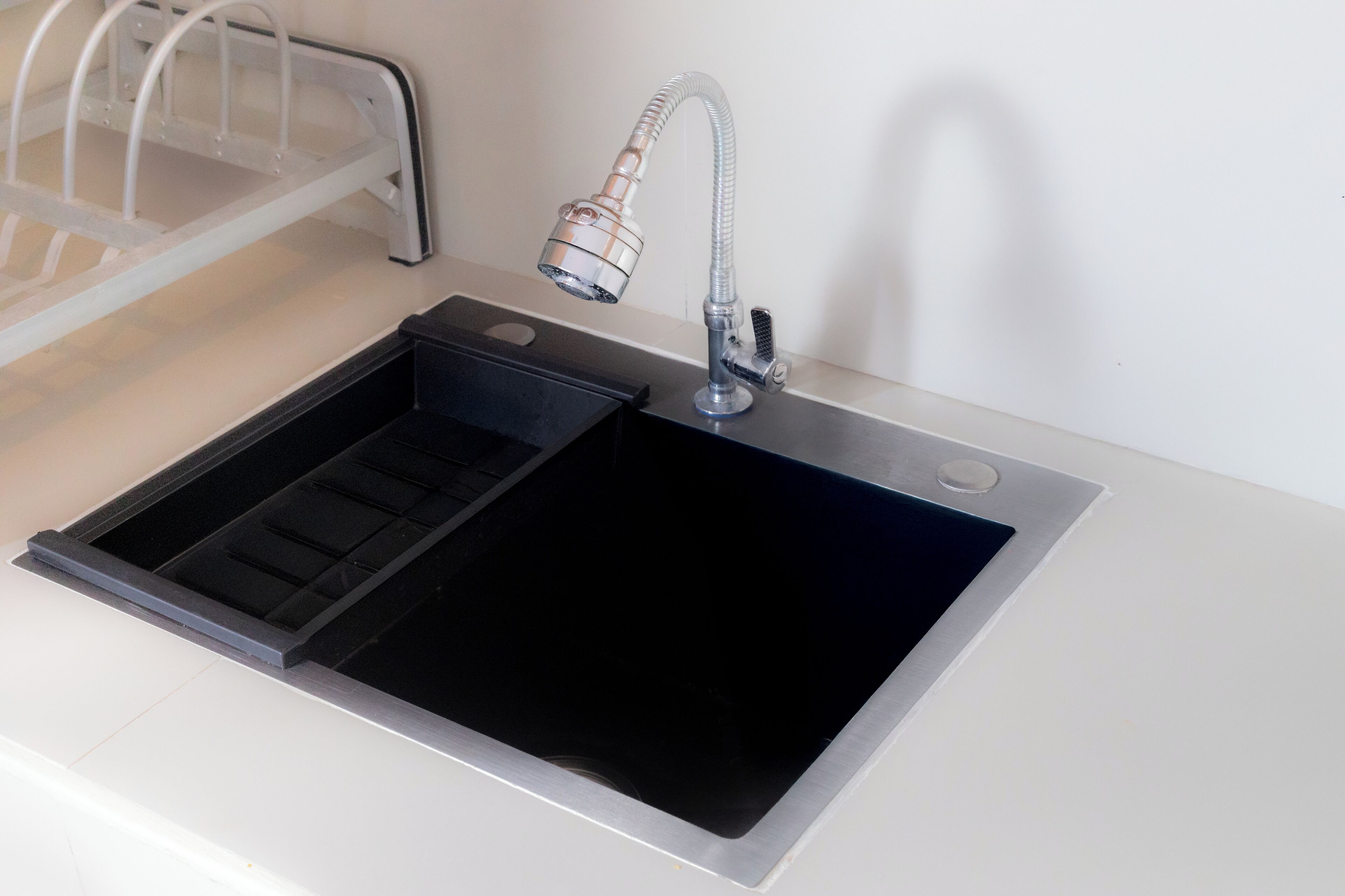 Una cocina moderna con un lavamanos negro, grifo de acero inoxidable y un escurreplatos integrado.