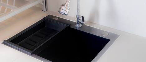 Una cocina moderna con un lavamanos negro, grifo de acero inoxidable y un escurreplatos integrado.