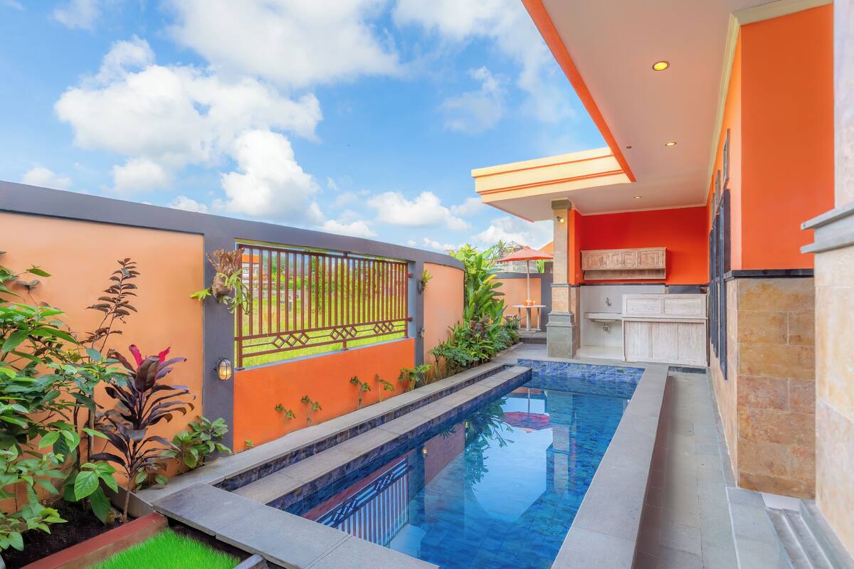 A swimming pool with a stone-lined edge, surrounded by a garden with various plants and a metal gate.