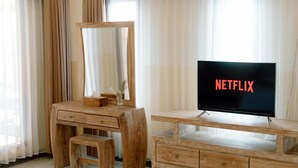 Una toeletta in legno con uno specchio, una televisione che mostra 'NETFLIX' e uno sgabello.