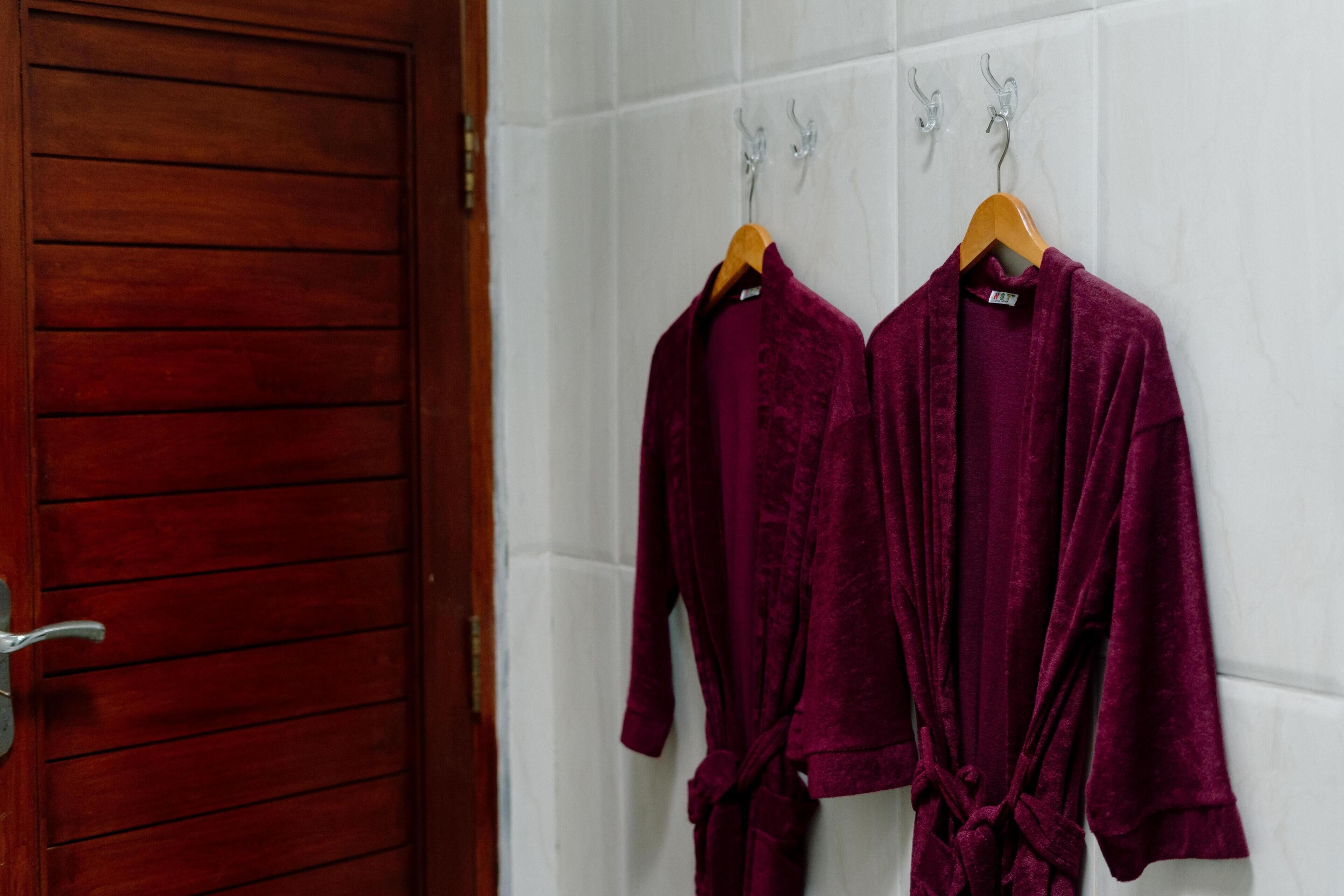 Two velvet robes hanging on a white tiled wall.