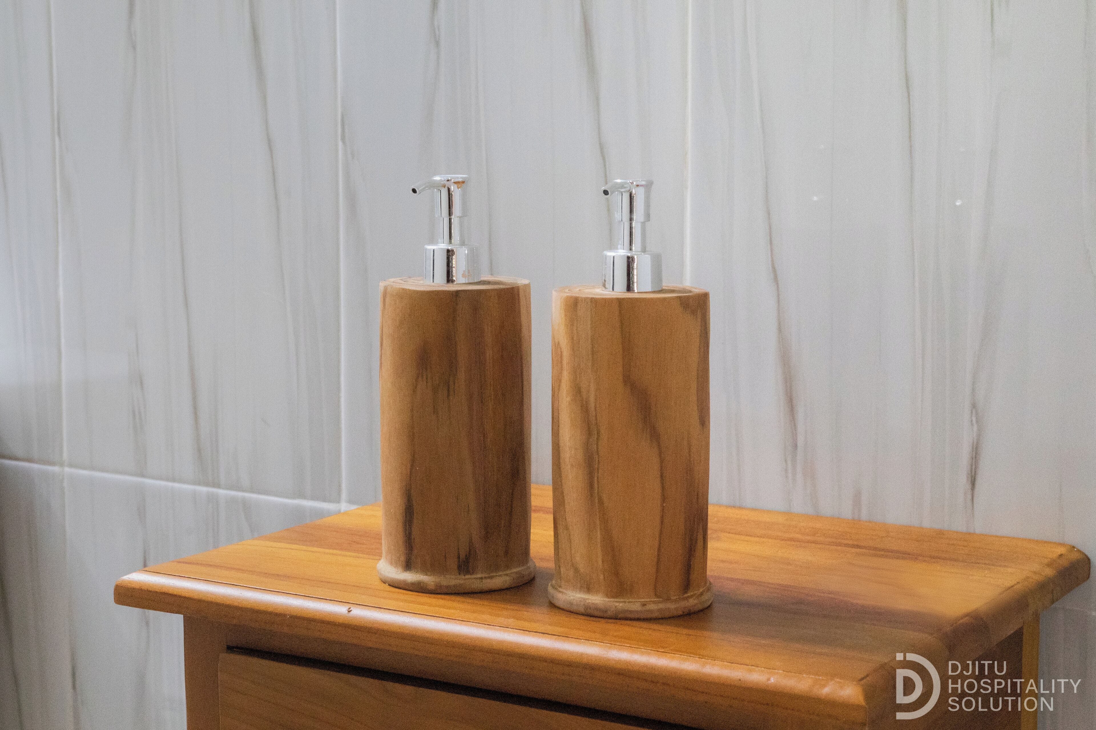 Two wooden dispensers on a wooden countertop against a marble wall.