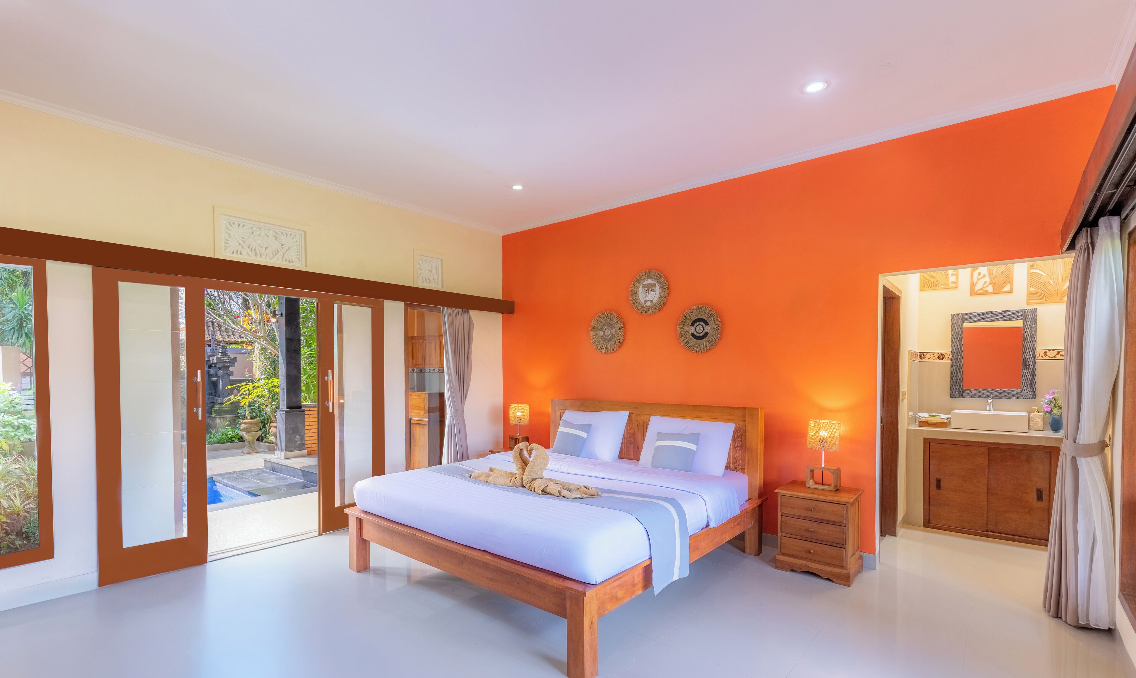 Un dormitorio con cama, mesitas de noche, baño con lavamanos y vistas al exterior.