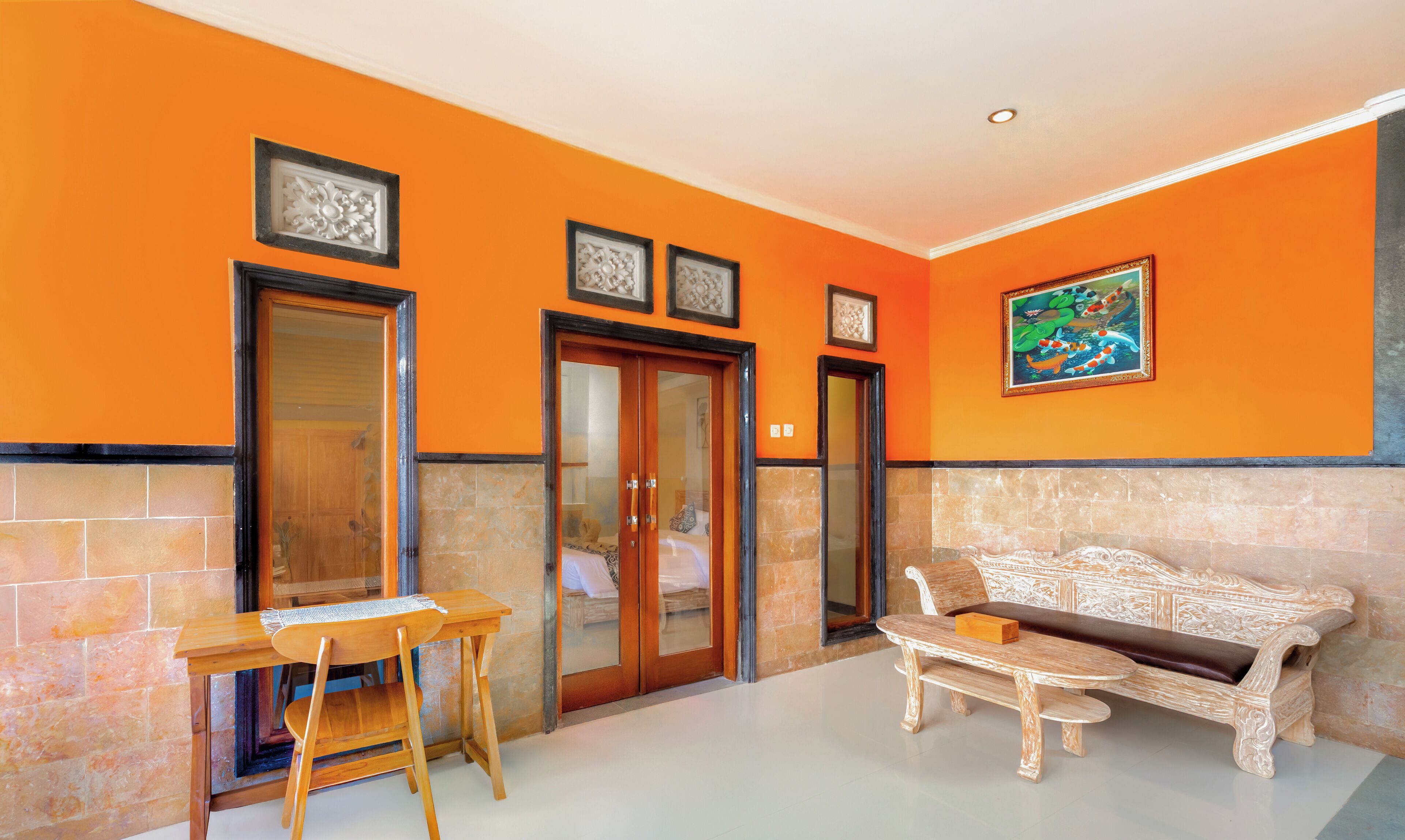 Un vestíbulo de hotel con una pared naranja, un escritorio de madera, un banco acolchado y una puerta que da a un dormitorio.