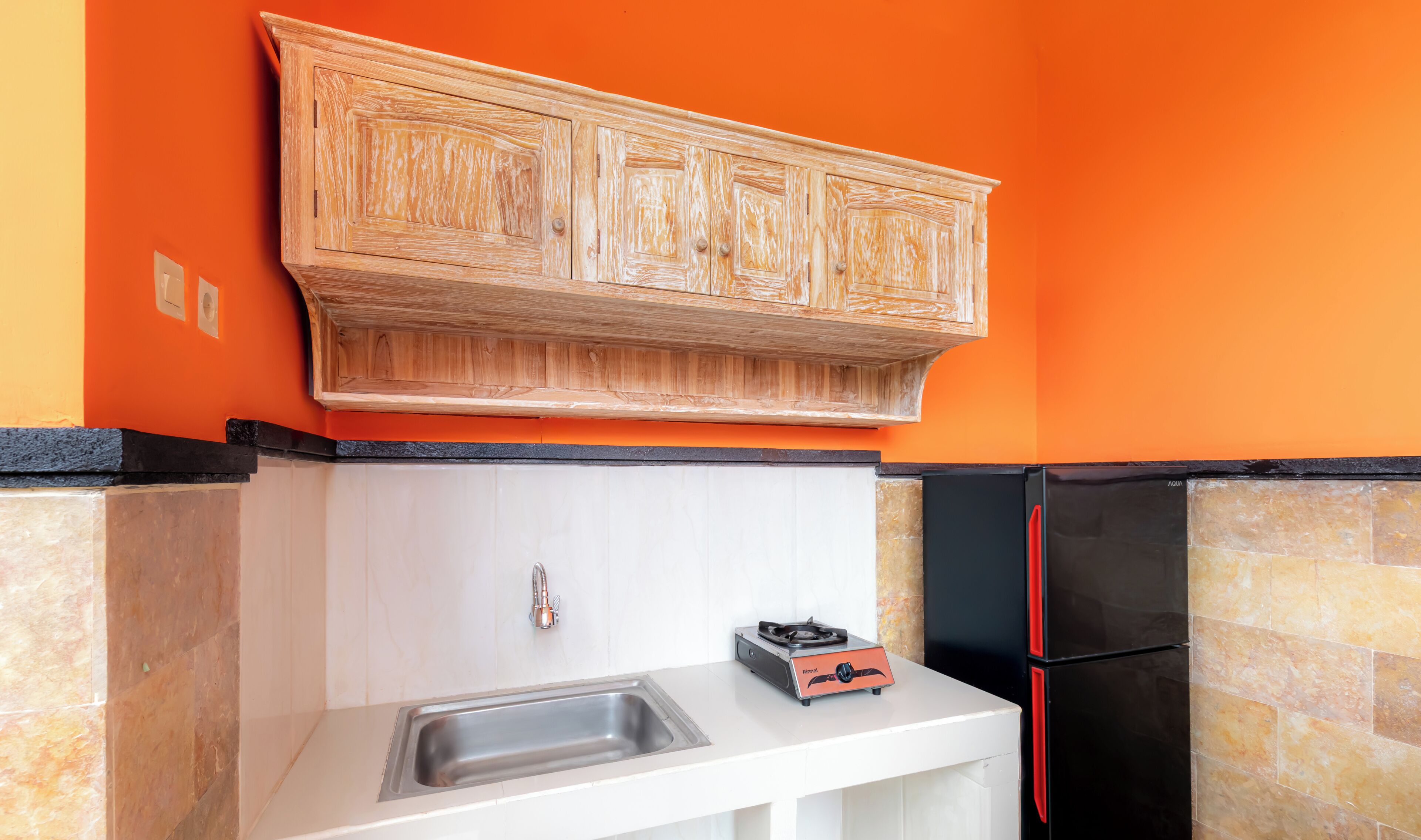A kitchen with a wooden cabinet above a white countertop, a sink, a gas stove, and a black refrigerator.