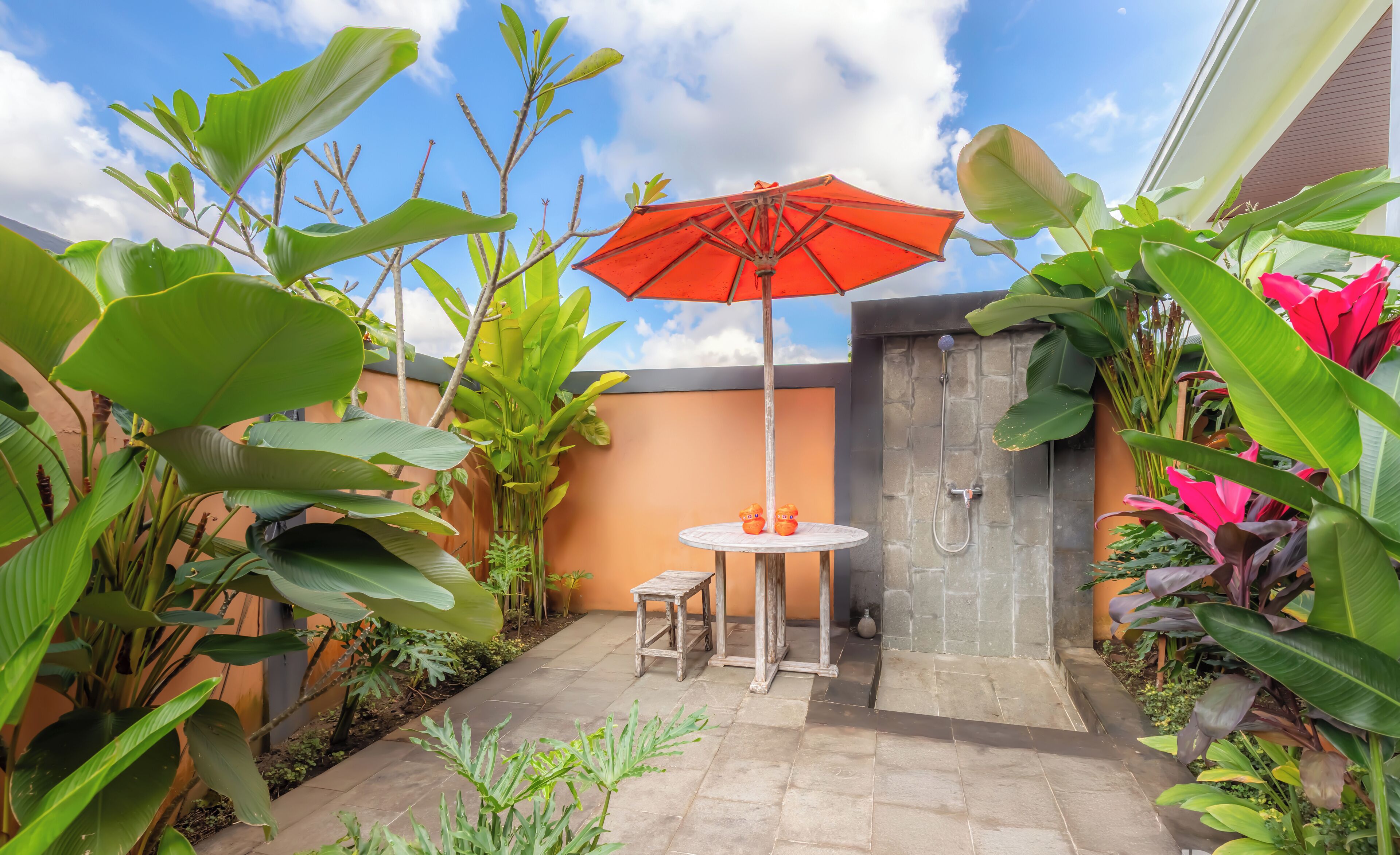 A patio area with a stone wall, a small round table, two chairs, and an orange umbrella.