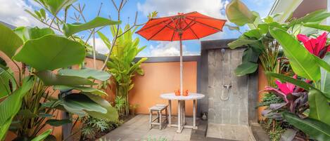 A patio area with a stone wall, a small round table, two chairs, and an orange umbrella.