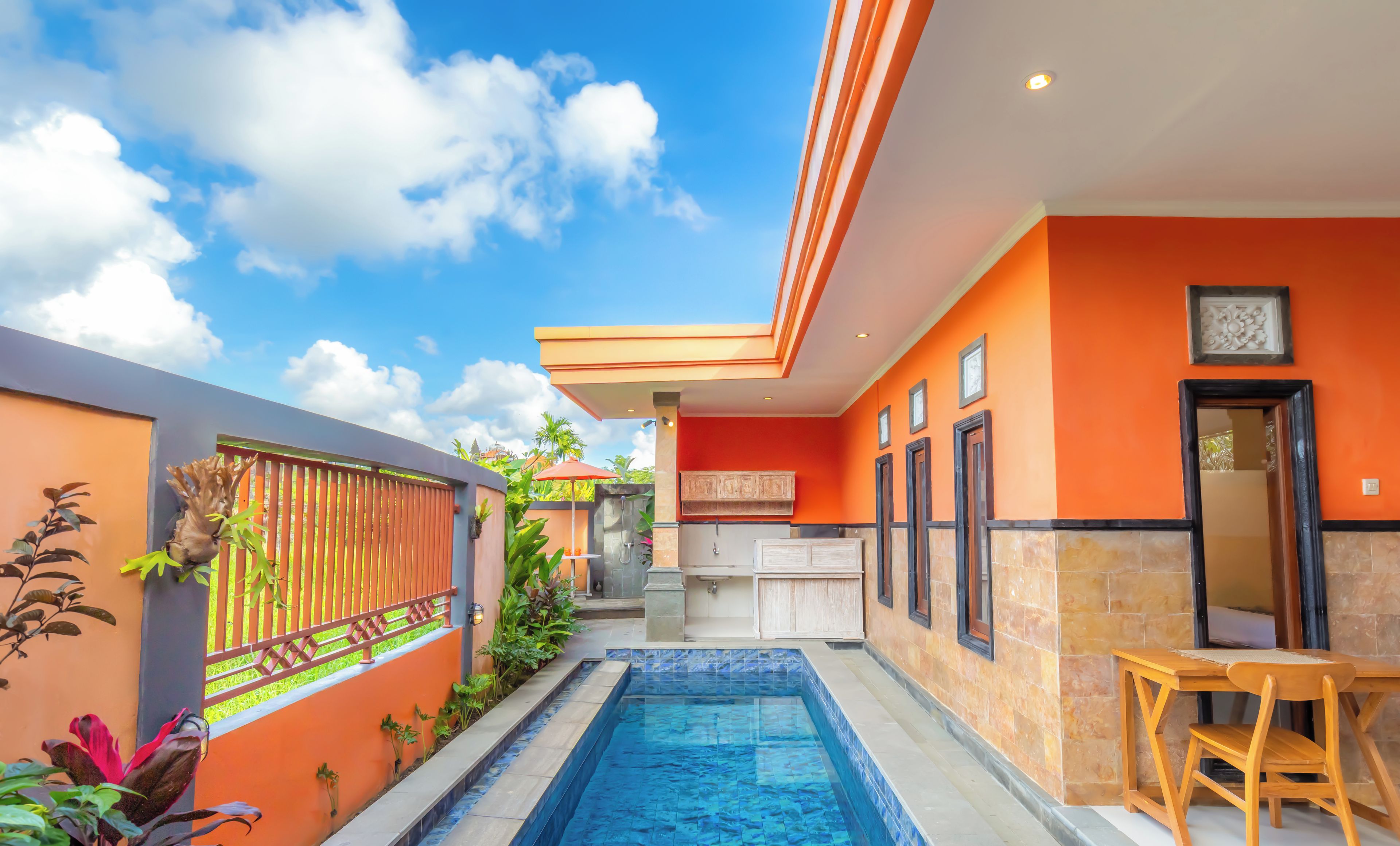Un espace piscine moderne avec une piscine à l’eau d’un bleu limpide, entourée de murs orange et d’une terrasse en bois.