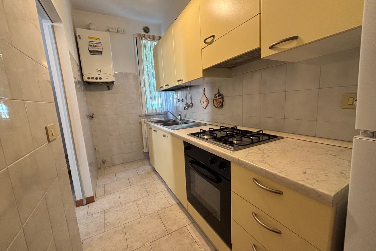 A compact kitchen with a gas stove, oven, and sink, featuring light-colored cabinets and a tiled backsplash.
