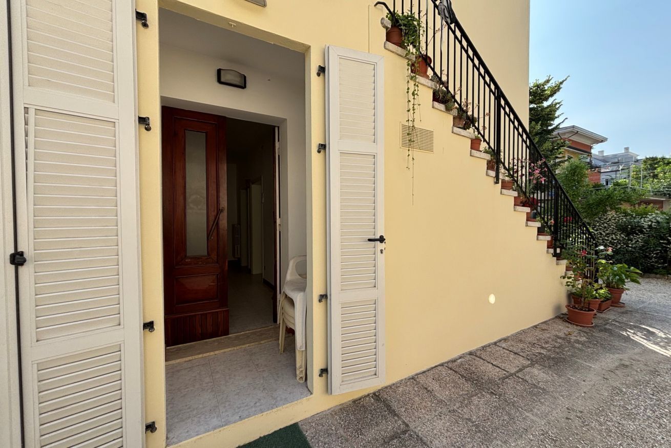 A building with a wooden door, a white shutter door, and a staircase with potted plants.