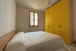 Une chambre à coucher avec un lit, une fenêtre avec des rideaux, un radiateur et une armoire jaune.