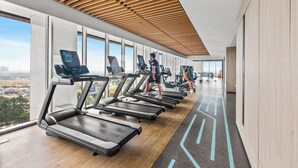 A modern gym with treadmills aligned along a wall with large windows offering a city view. - Branca by Kozystay - Alam Sutera (Tangerang)