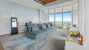 A modern living room with a grey sectional sofa, a large window offering a city view, and a children's play area with a toy truck. - Branca by Kozystay - Alam Sutera (Tangerang)