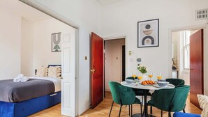 A modern bedroom with a bed, a dining area with a table and chairs, and a kitchen in the background. - Charming 1BR in the Heart of Soho and Fitzrovia (London)