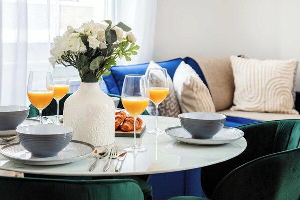 Une table mise pour le petit-déjeuner, avec une nappe et une place pour deux personnes, comprenant des bols, des assiettes, des couverts et des verres de jus d’orange.