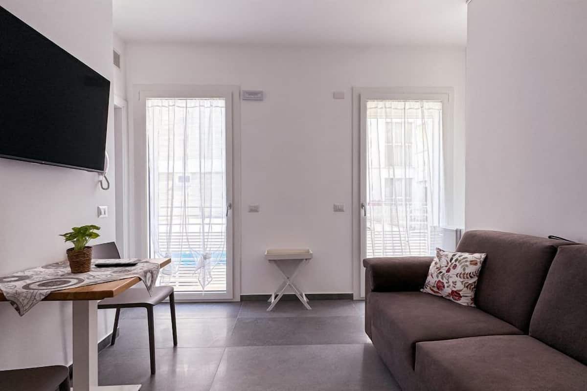 Uma sala de estar moderna com um sofá cinzento, uma mesinha e uma TV fixada na parede.