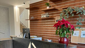Un mostrador de recepción de hotel con un diseño moderno, que incluye un logotipo, una computadora y una planta en maceta.