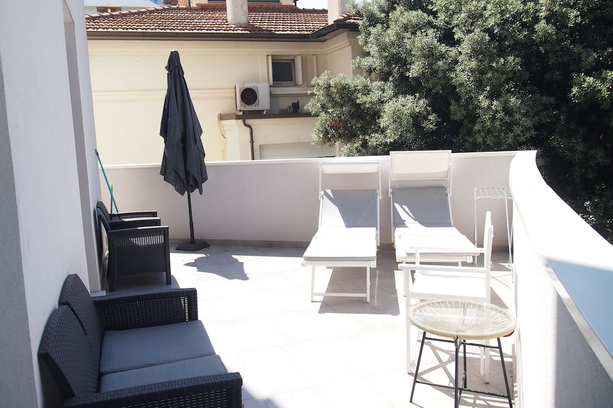 Terraço no telhado com cadeiras de banho brancas, um sofá de vime e uma pequena mesa.