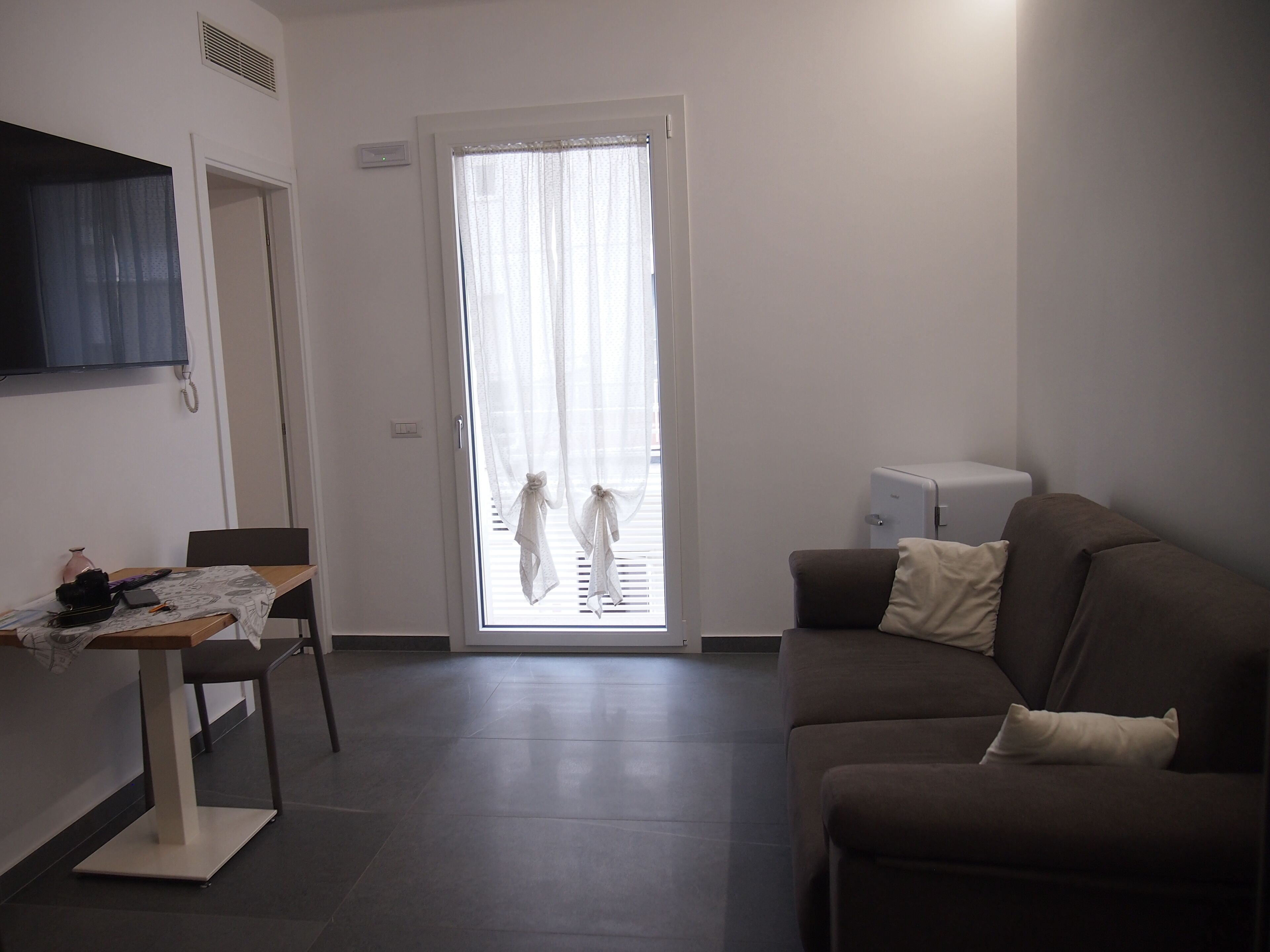 A modern living room with a brown sofa, a small table with a lamp, and a television mounted on the wall.