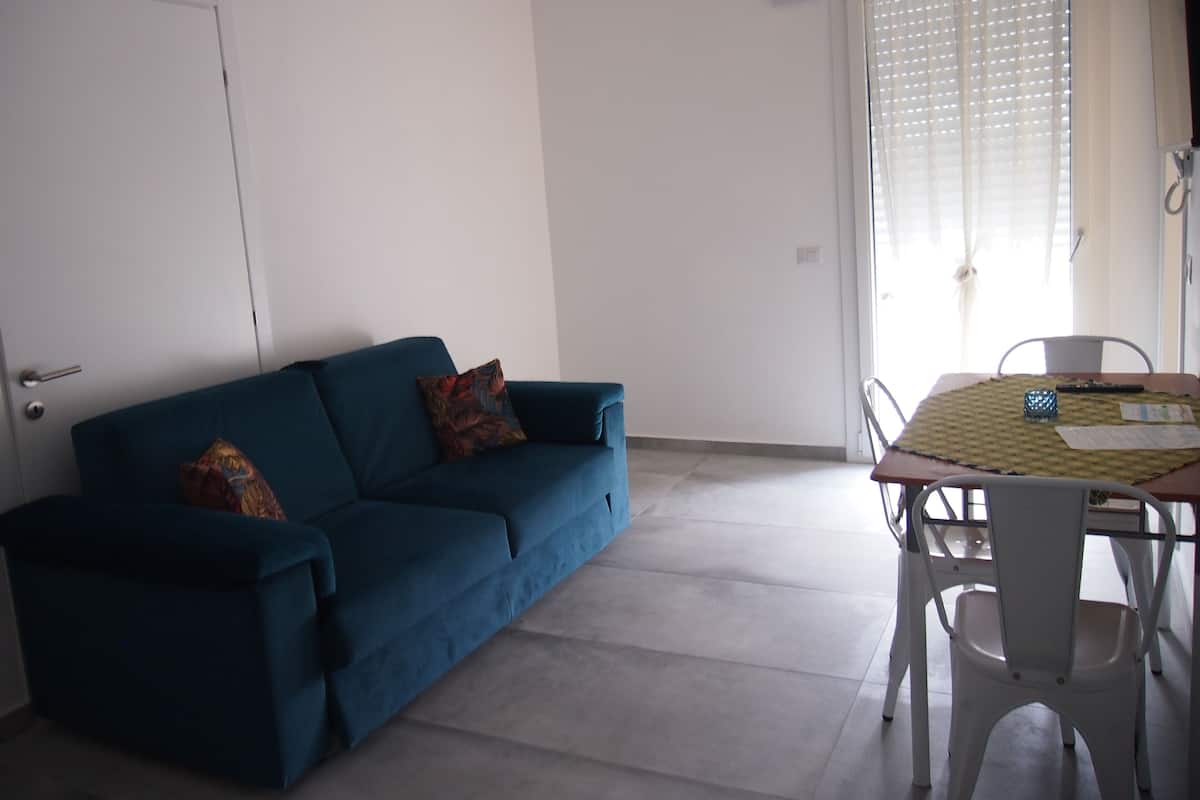 Um quarto com um sofá azul, uma mesa de jantar com cadeiras e uma porta.
