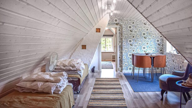 Un dormitorio acogedor en el ático, con techo inclinado, cama, una mesita y una silla.