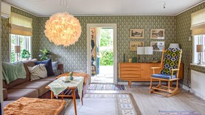 Una sala de estar acogedora con un sofá, una silla de madera, una mesa con un florero y una lámpara colgante.