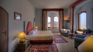 Una habitación de hotel con una cama, dos lámparas de noche, un sofá, una silla y vistas a la ciudad a través de amplios ventanales.