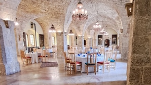 Un amplio salón con altos arcos de piedra, mesas de madera dispuestas para comer y candelabros colgantes.