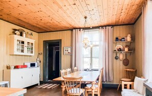A wooden-paneled room with a dining table, chairs, a kitchen area with cabinets, and a window with curtains. - Beautiful home in Grimsås (Grimsås)