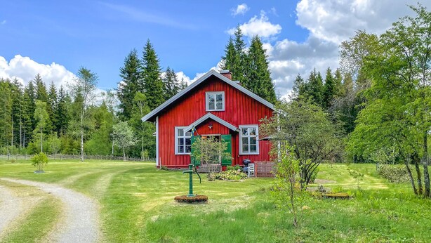 Een rode houten woning met schuin dak, omringd door een verzorgd gazon en bomen.
