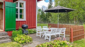 Een terras met een barbecue, witte stoelen en een tafel.