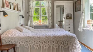 Een slaapkamer met een groot bed, een garderobe, een stoel en een raam met gordijnen.