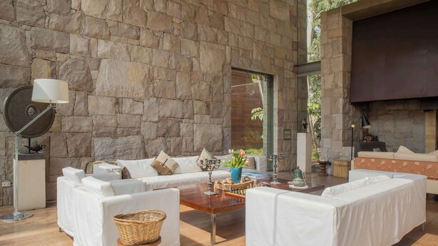 Una sala de estar moderna con paredes de piedra, sofás blancos, una mesa de centro de madera y una chimenea.