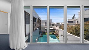 Une chambre moderne dotée de grandes fenêtres du sol au plafond, offrant une vue sur une piscine, et d’un balcon avec une balustrade.