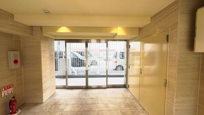 A hotel entrance with a fire alarm and extinguisher on the wall, a fire safety sign, and a view of parked cars through the glass doors. - Rakuyado Sanno (Osaka)