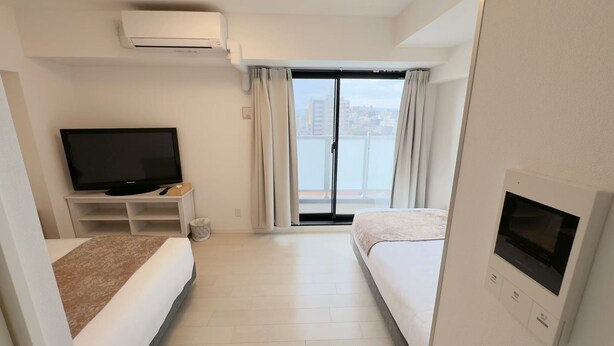 A hotel room with a TV, a sofa, a bed, a balcony with curtains, and a wall-mounted air conditioner. - Rakuyado Sanno (Osaka)