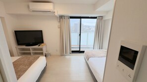 Ein Hotelzimmer mit Fernseher, Sofa, Bett und einem Balkon mit Vorhängen sowie einer Wand-Klimaanlage.