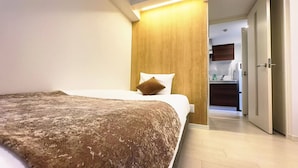 A hotel room with a large bed, a wooden headboard, and a view into the kitchen area. - Rakuyado Sanno (Osaka)