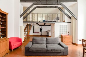 A spacious living room with a grey sofa, a red armchair, and a wooden cabinet. A staircase leads to an upper level. - A 5 passi dalla Fontana di Trevi – Loft romano del XVII secolo! (Rome)