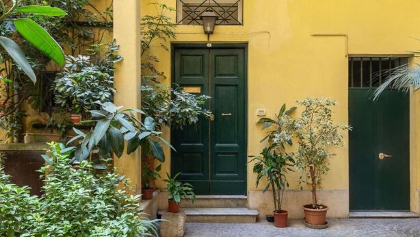 Un bâtiment jaune avec une porte verte et des plantes en pot.