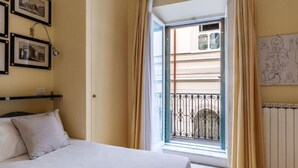 Une chambre à coucher avec un lit, une fenêtre avec des rideaux, un radiateur et des tableaux encadrés accrochés au mur.