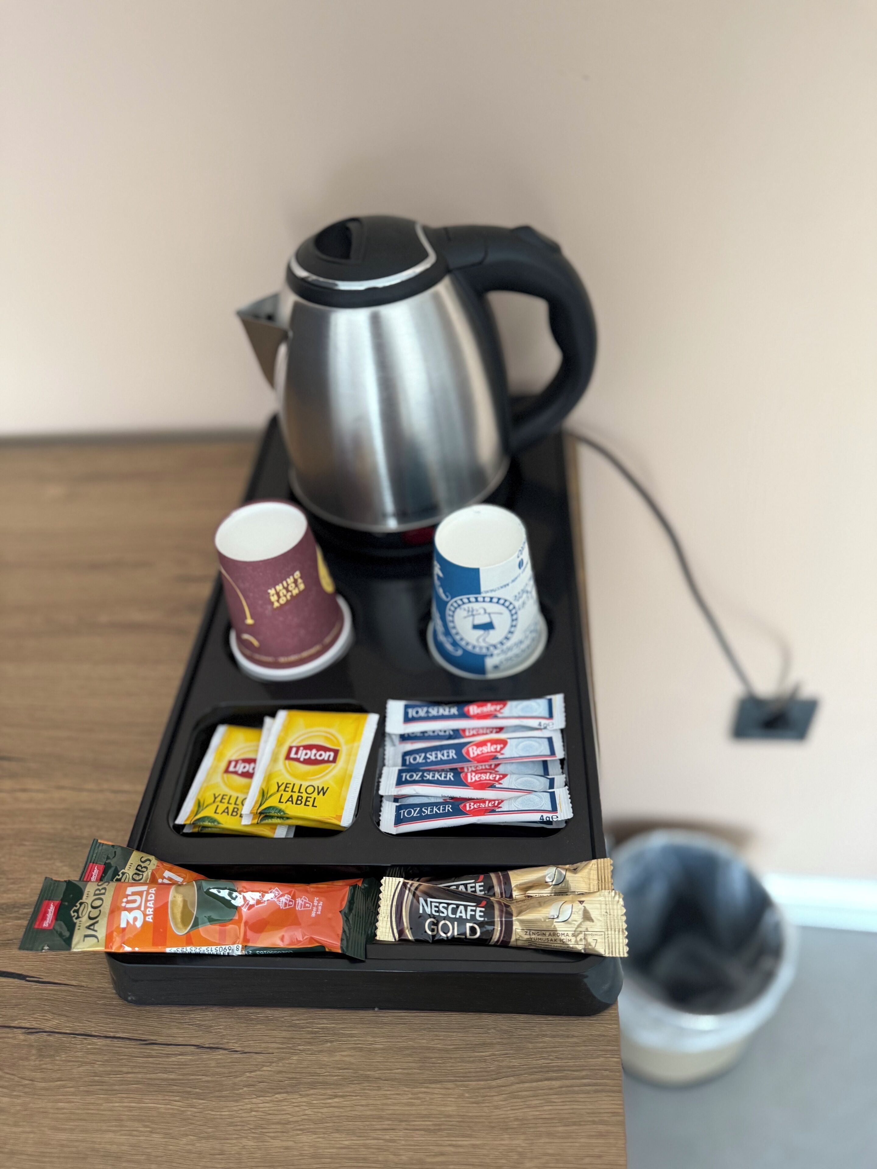 A coffee station with a kettle, cups, and coffee pods on a tray.