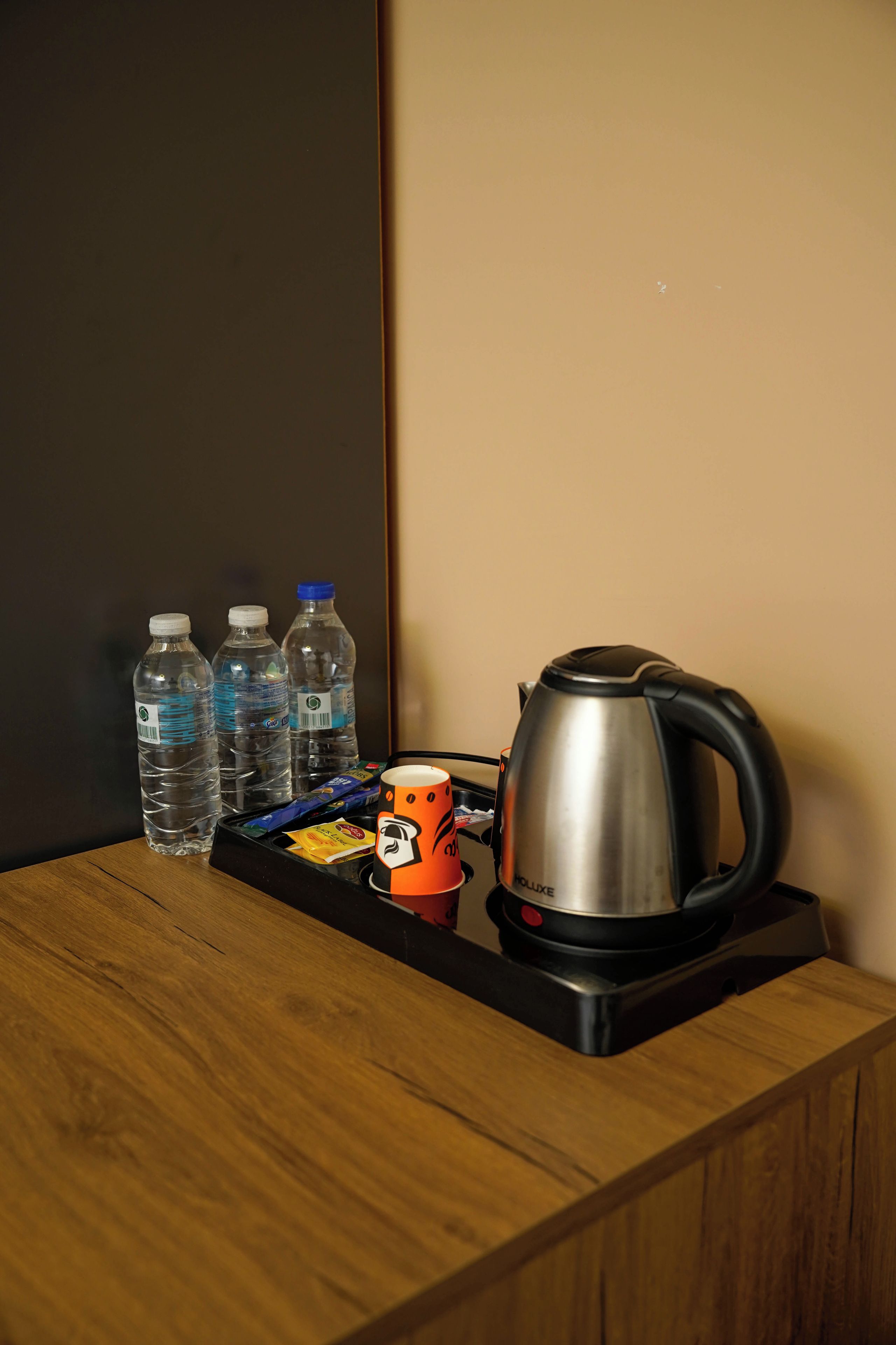 A kitchenette with a kettle, water bottles, and a mug on a wooden table.