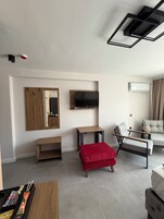 A modern living room with a flat-screen TV, a wooden cabinet with a mirror, a red ottoman, a sofa, and a coffee table.