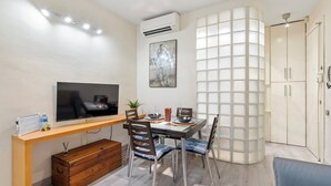 A modern living room with a TV, dining table, chairs, a sofa, a wooden chest, and a decorative wall panel.