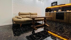 Een moderne woonkamer met een bank, een houten salontafel en een keuken met een houten aanrecht en apparatuur.