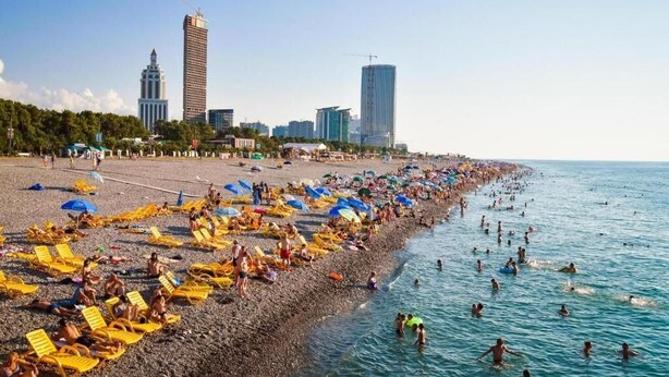 Een strand met gele ligbedden en mensen die in het water zwemmen.