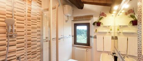 A bathroom with a shower, toilet, bidet, and sink. There is a window providing natural light and a view of the outdoors.